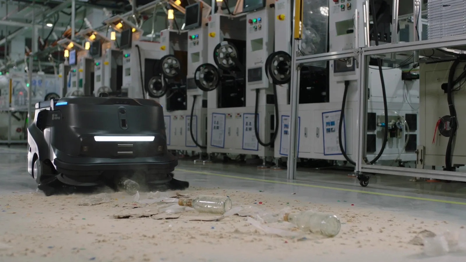 PUDU MT1 sweeping scattered packaging debris from a factory floor between machinery